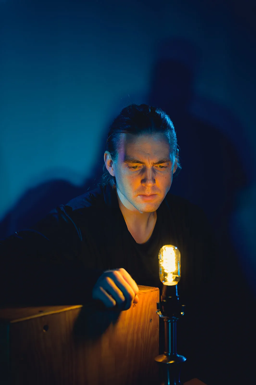 Robin McGinness in Alceste with In Series — face lit by a single lamp in blue darkness