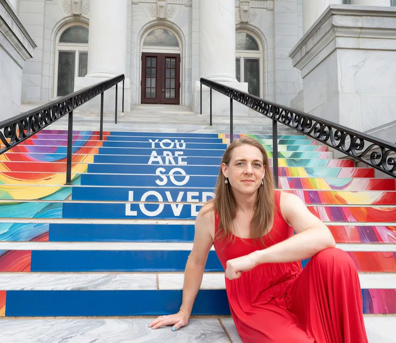 Robin McGinness in a red dress on painted capitol steps reading 'You Are So Loved'
