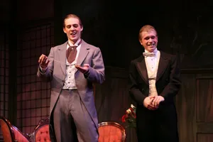 Robin McGinness in a grey Victorian morning suit, admiring a pocket watch beside a performer in white tie