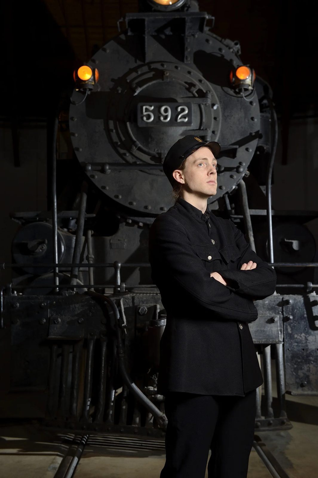 Robin McGinness as the stationmaster in The Ghost Train (Peabody Chamber Opera), arms folded before locomotive 592